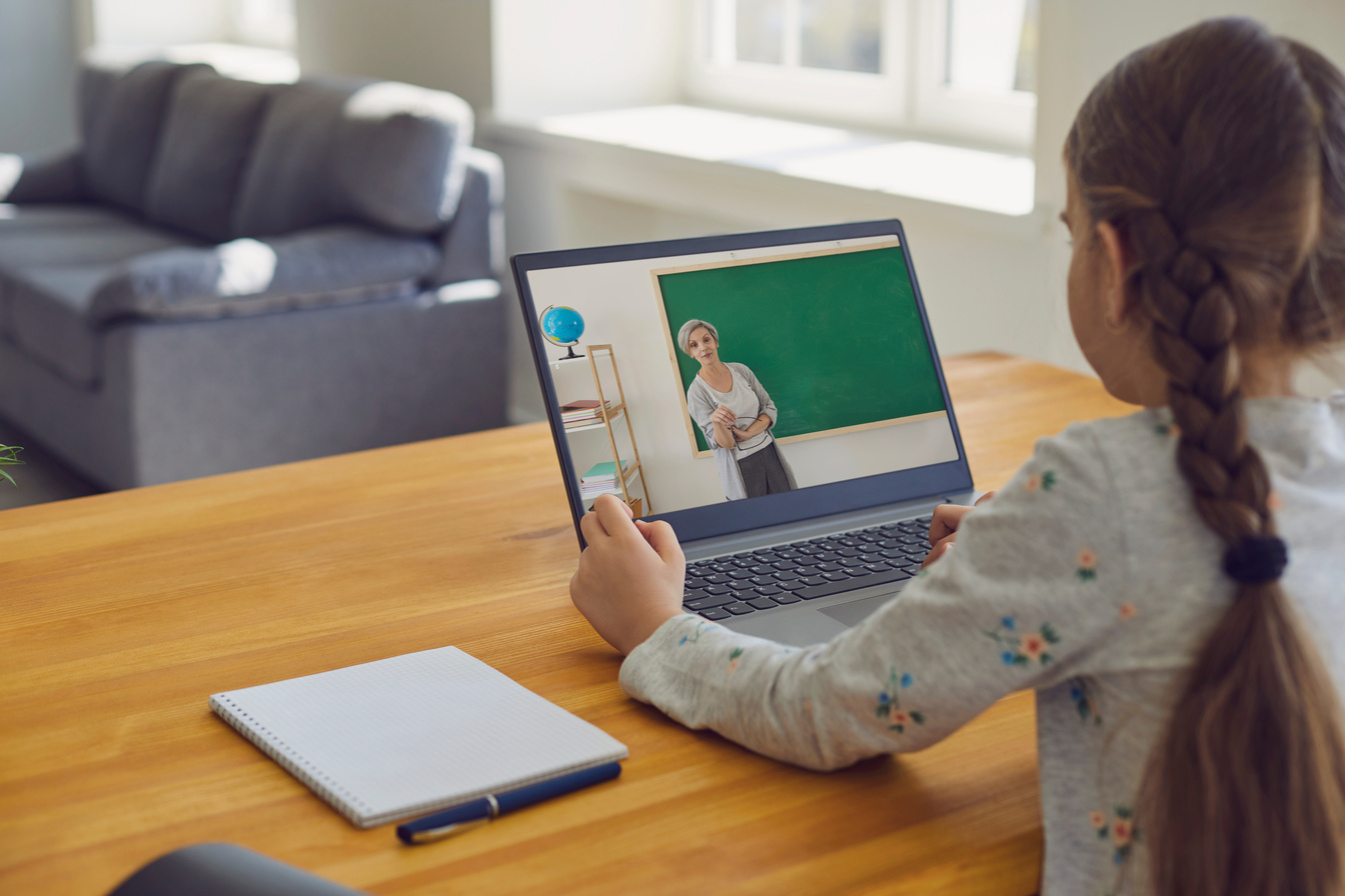 Online Education.Little Girl Listens to the Lesson Online. on the Laptop Screen, an Older Woman Teacher Is at School. School Online.